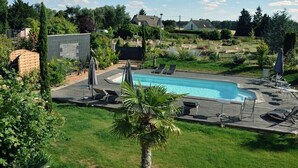 A rectangular swimming pool with a wooden deck and lounge chairs, surrounded by greenery and a clear sky. - Family chateau in the heart of an estate (Flacey)