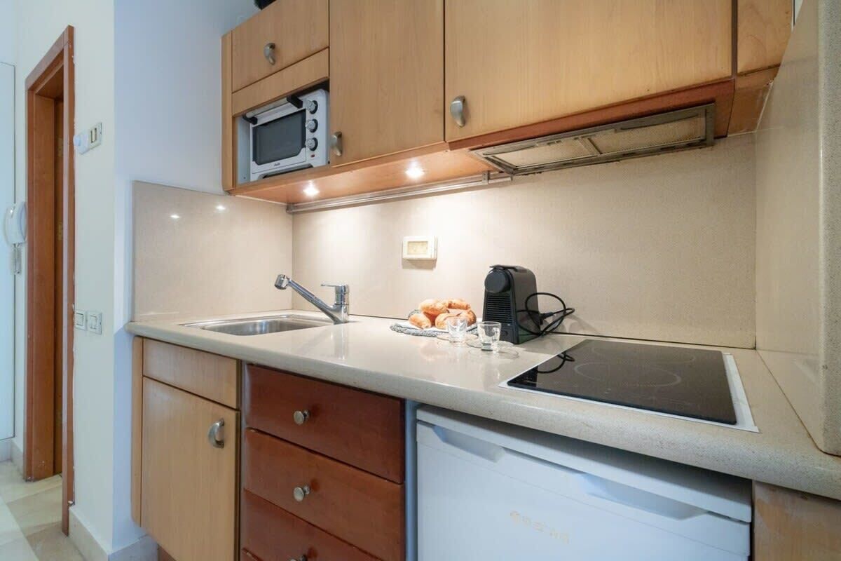 A compact kitchen with wooden cabinets, a microwave, a sink, and a built-in dishwasher.