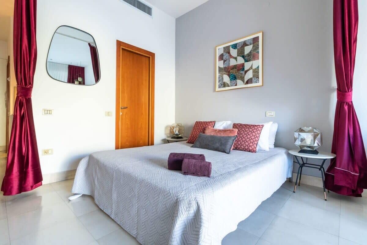 Une chambre à coucher bien rangée, avec un grand lit, une table de chevet avec une lampe, un miroir et une porte.