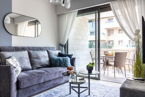 Un salon moderne avec un canapé gris, une table basse ronde et une grande fenêtre avec des rideaux.