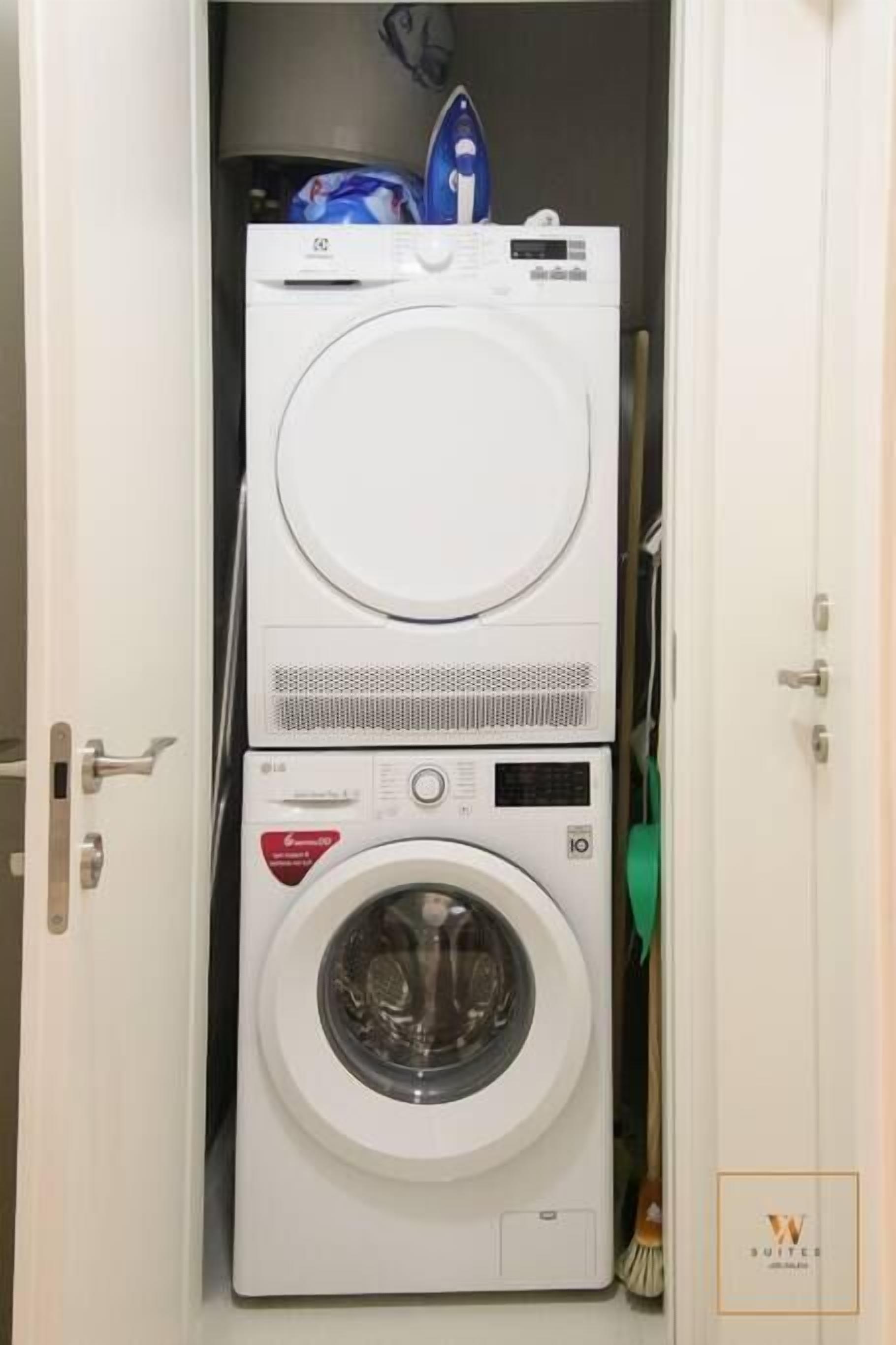 Een kleine, witte wasruimte met een voorlader wasmachine en droger die verticaal boven elkaar staan.