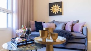 A modern living room with a grey sofa, a round coffee table, and decorative items including a tray of macarons and wine glasses. - King David Luxury 2BR/Parking/View Old City (Jerusalem)