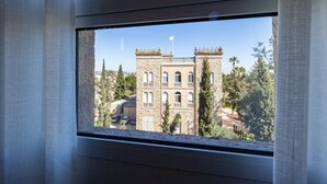 A window with a view of a stone building with arched windows and a flag on top. - King David Luxury 2BR/Parking/View Old City (Jerusalem)