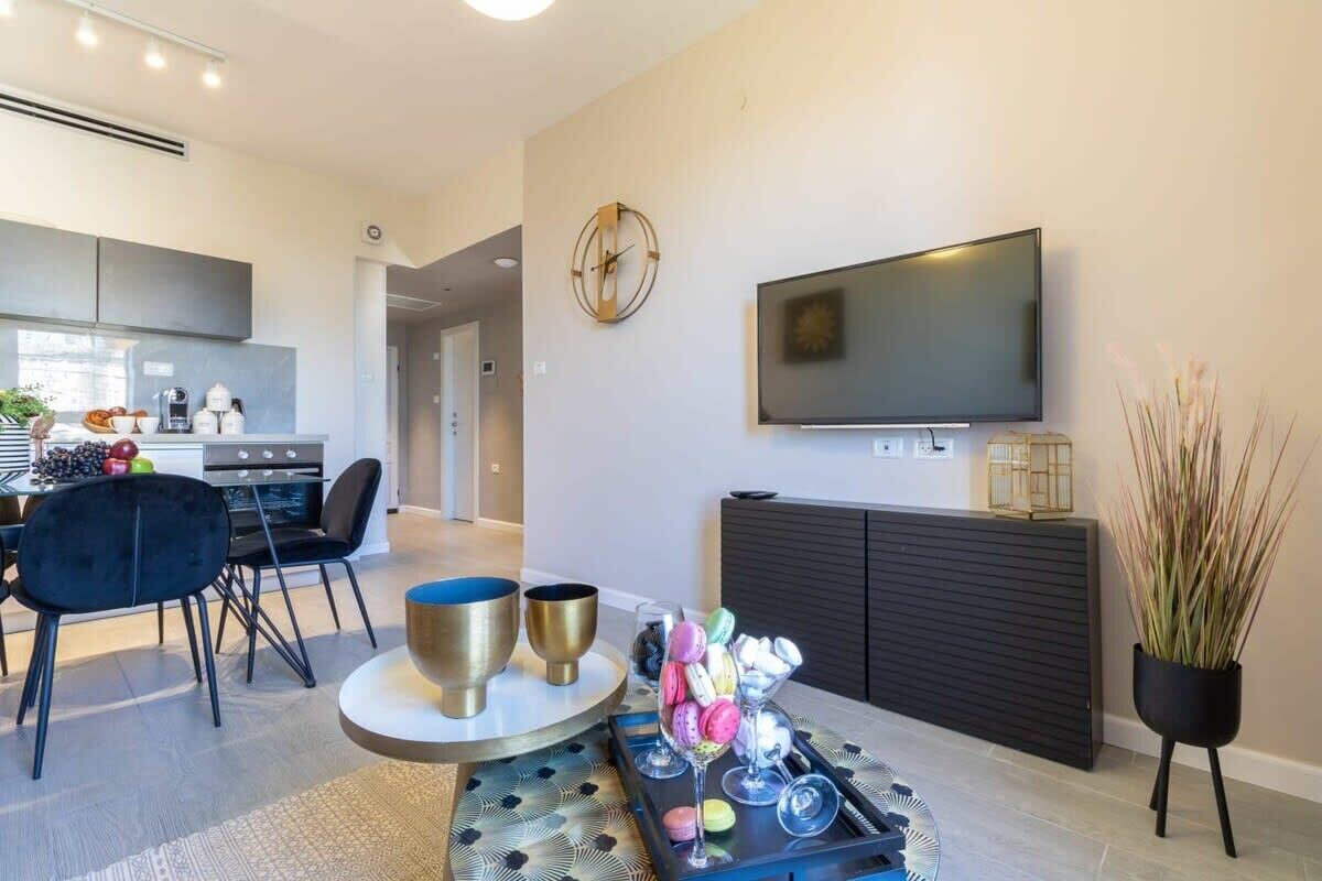 A modern living room with a flat-screen TV, a dining area with a kitchen in the background, and a decorative tray with macarons.