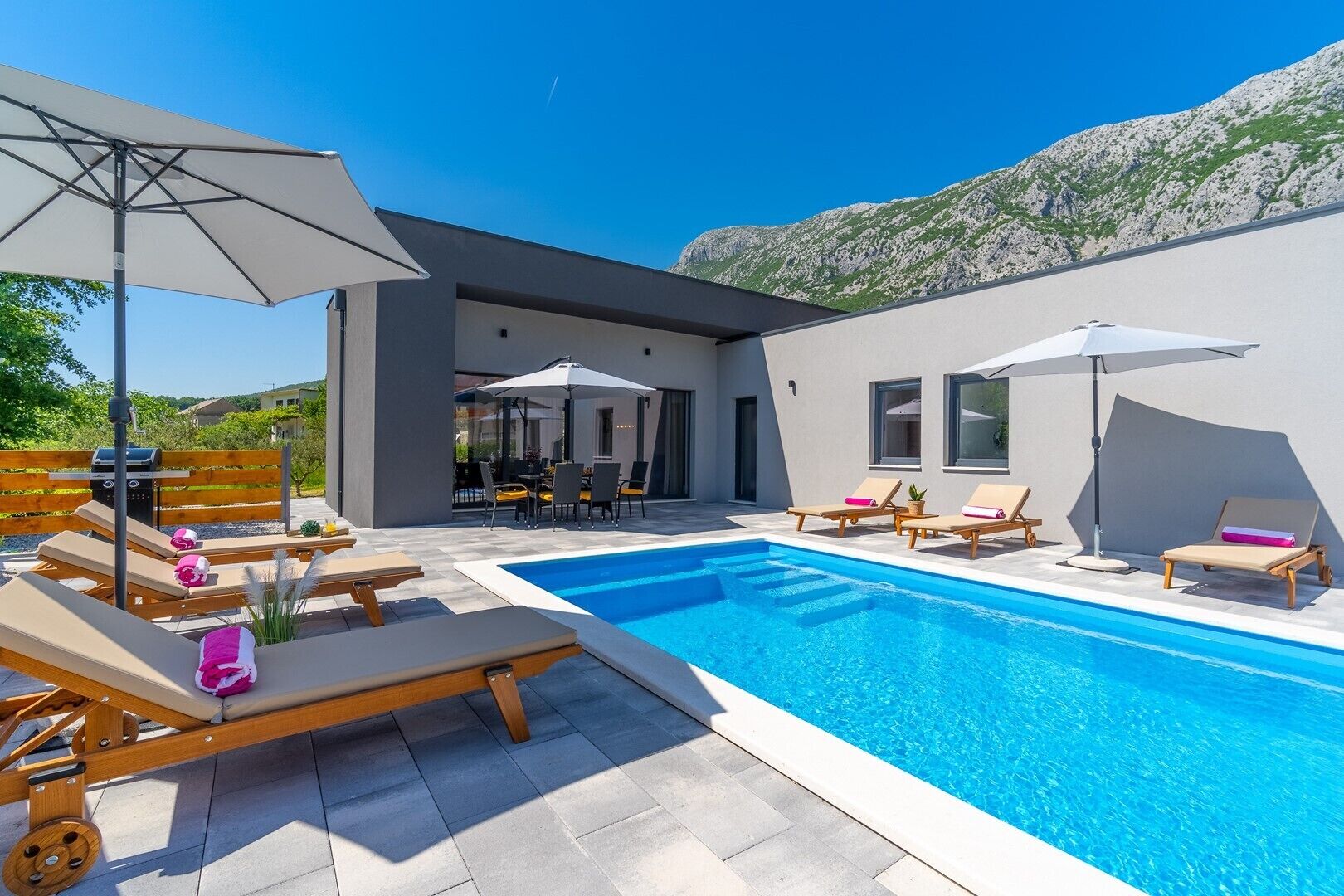A modern outdoor pool area with lounge chairs and umbrellas, surrounded by a contemporary building with large windows.