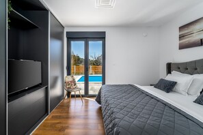 Ein modernes Schlafzimmer mit einem großen Bett, einem Fernseher und einer Schiebetür zu einem Pool.