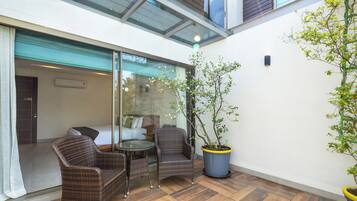 Guest room with a comfortable bed, sofa, and dining area, featuring a potted plant and natural light.
