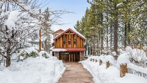 Una cabaña de madera con techo rojo, rodeada de árboles cubiertos de nieve y un sendero nevado que conduce a la entrada.