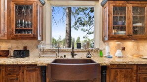 Una cocina con armarios de madera, encimera de granito, pileta y ventana con vista a árboles.