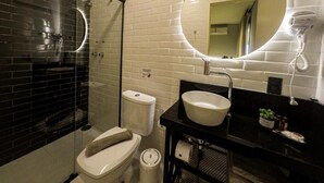 A modern bathroom with a glass-enclosed shower, a white toilet, a black sink, and a round mirror with a light. - Castro's Hotel (Telemaco Borba)