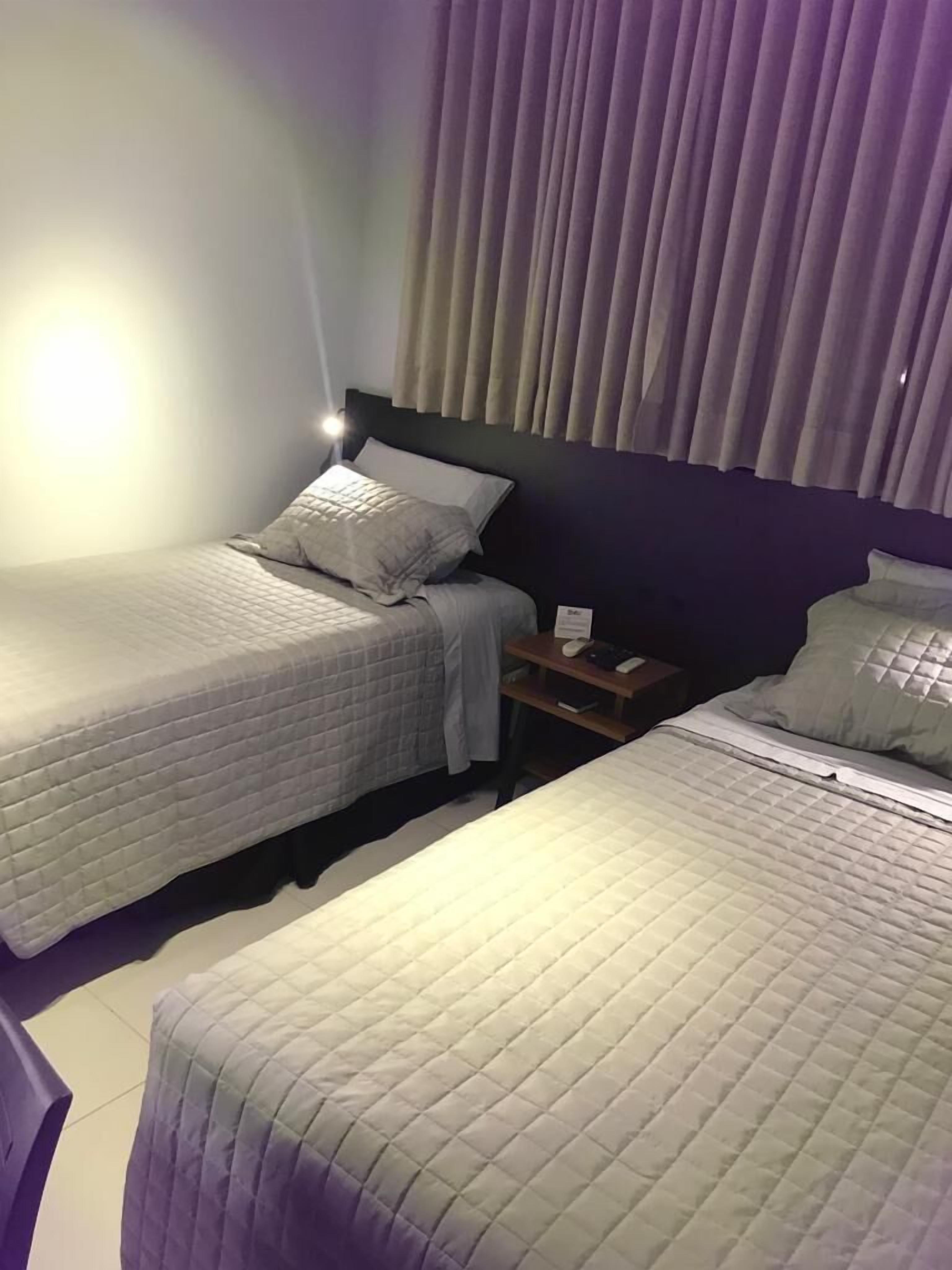 Une chambre d’hôtel avec deux lits simples, une table de chevet et une lampe.