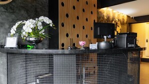 A reception desk with a clock, a flower arrangement, a coffee machine, and a television. - Castro's Hotel (Telemaco Borba)