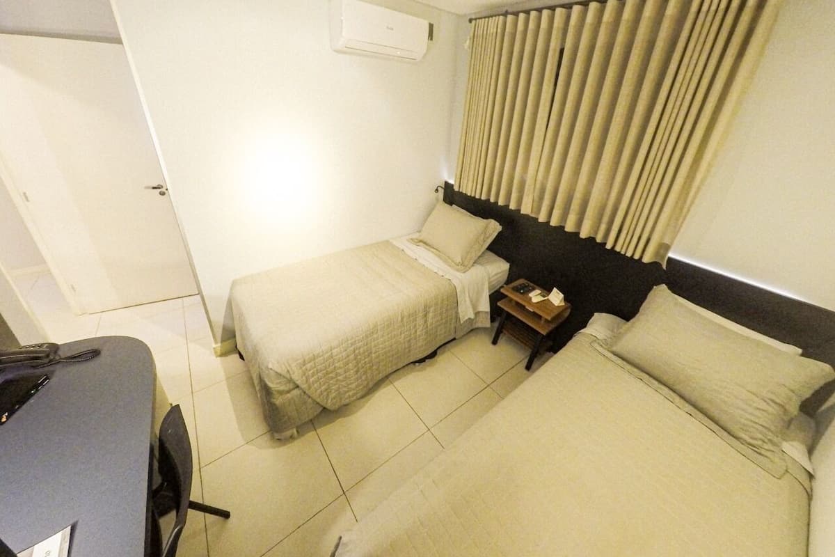 A hotel room with two beds, a desk, a chair, a nightstand, and a window with curtains.