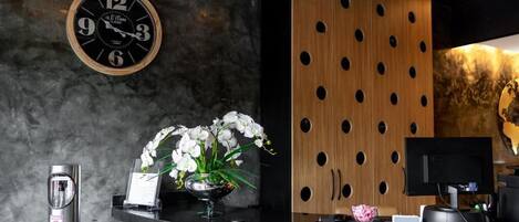 Un mostrador de recepción con un reloj, un jarrón de flores y una pared de paneles de madera moderna.