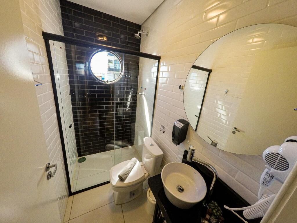A modern bathroom with a glass-enclosed shower, a white toilet, a sink with a mirror, and a hairdryer.