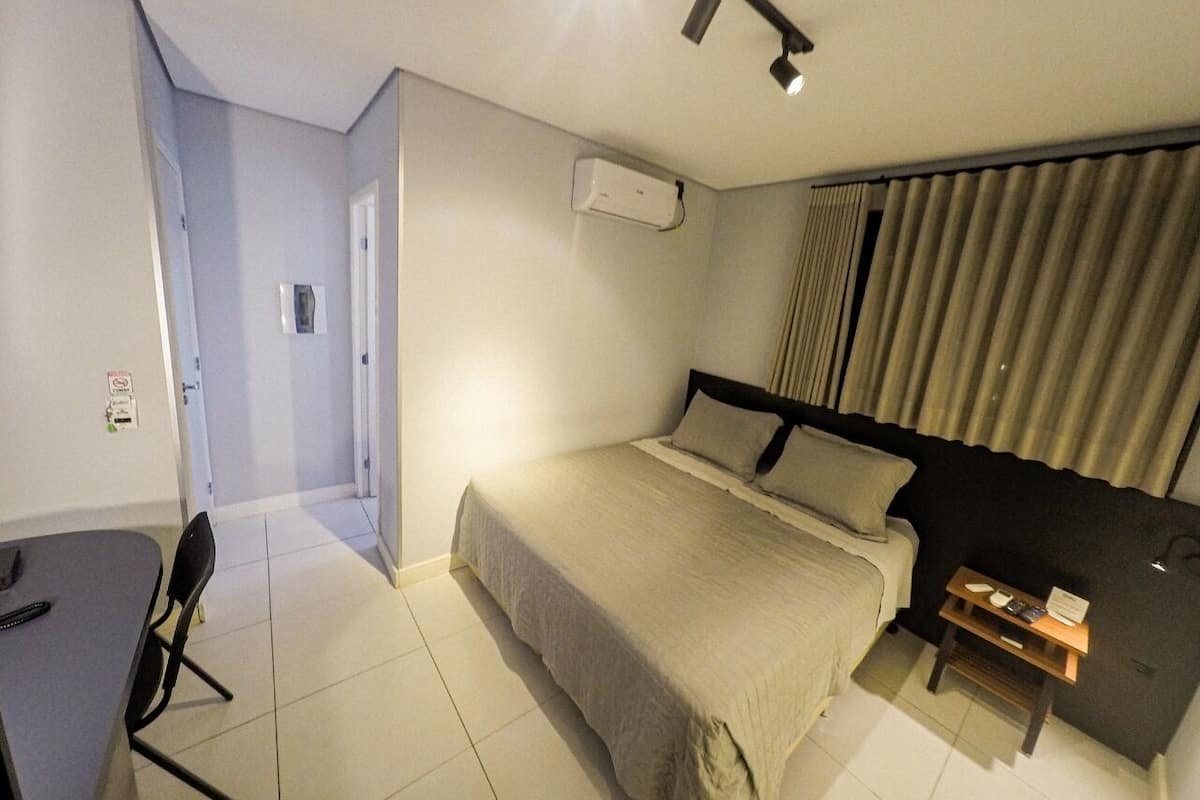 A hotel room with a bed, a desk, a chair, a nightstand, and a window with curtains.