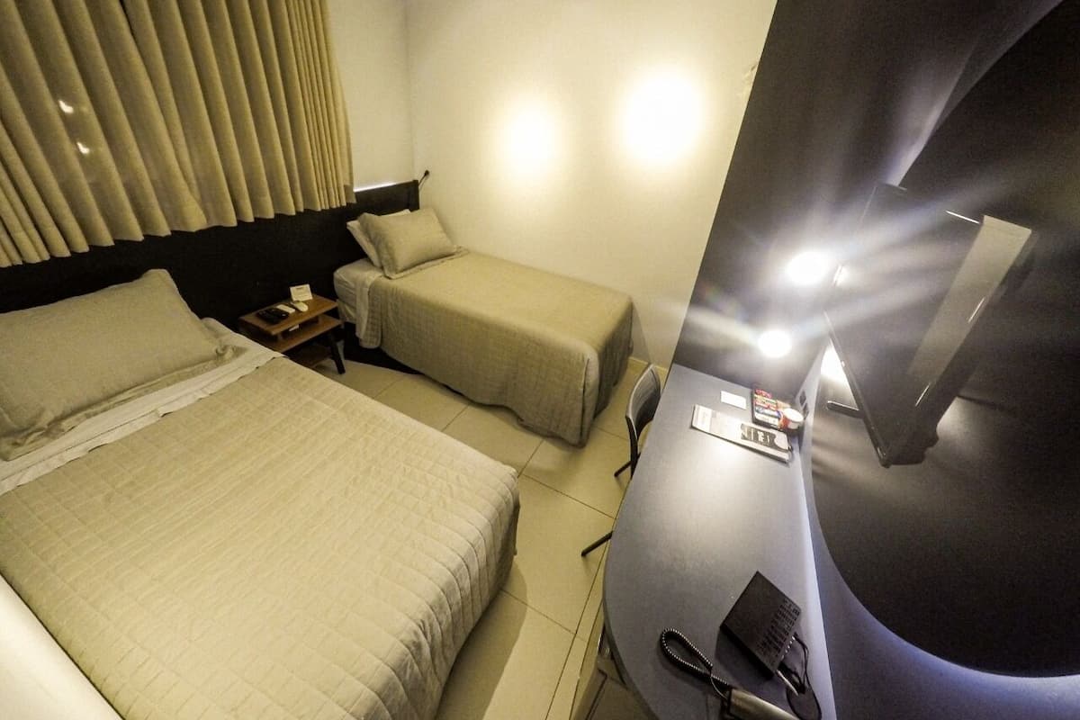 A hotel room with two beds, a desk, a chair, and a TV.