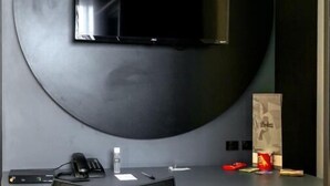 A modern room with a large circular wall-mounted TV, a small desk with a chair, a refrigerator, and a trash bin. - Castro's Hotel (Telemaco Borba)
