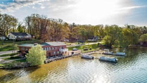 A lakeside property with a dock, boats, and a building with a red roof. - Lakefront Cottage with Hot Tub & Fire Pit (Fife Lake)