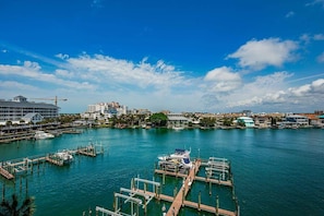 A marina with docked boats, a large building with a crane, and a cityscape in the background.