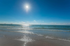 Une plage avec un ciel dégagé, une eau calme et une jetée visible au loin.