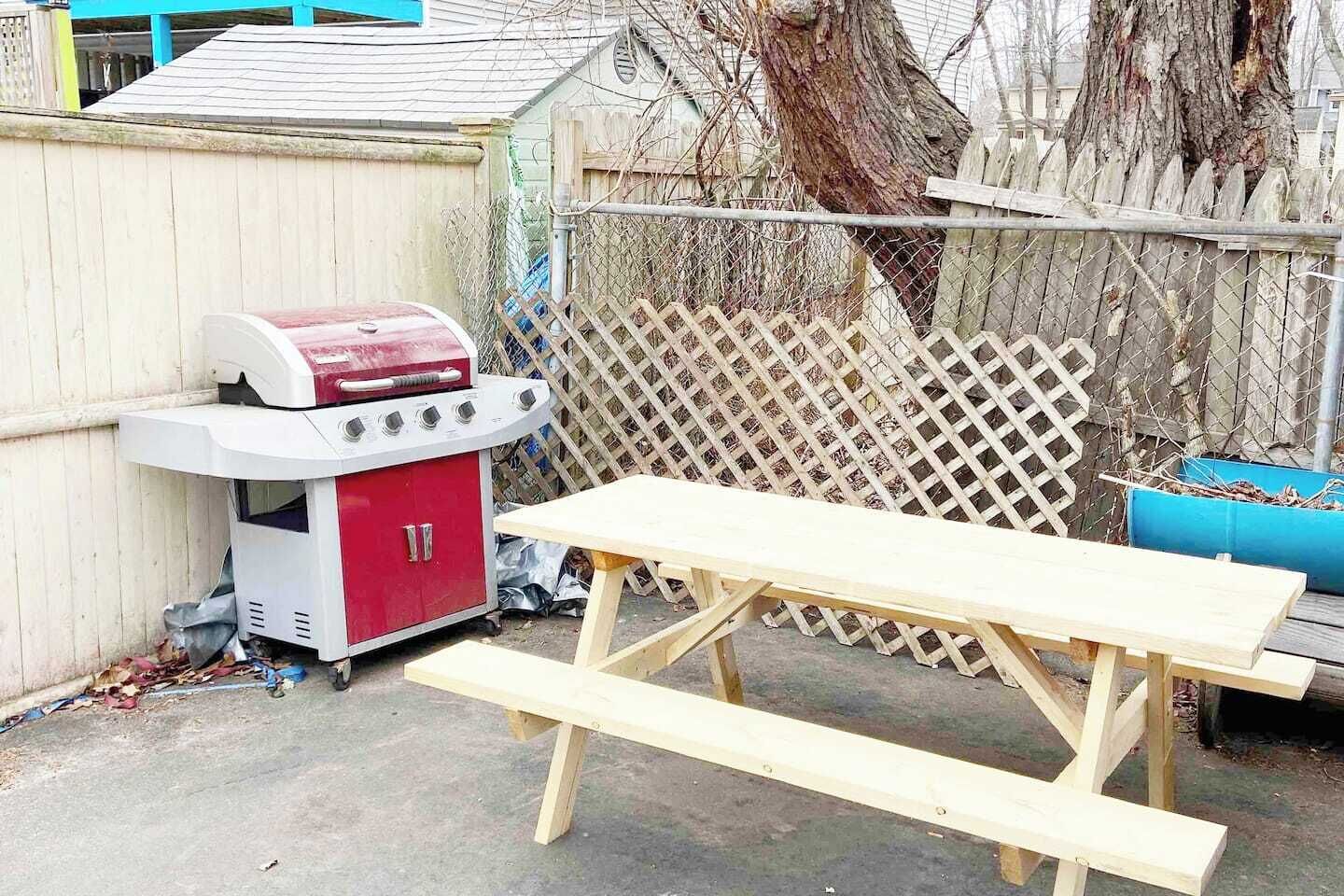 Un patio trasero con una parrilla, una mesa de picnic y una cerca de madera.