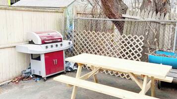 Un patio trasero con una parrilla, una mesa de picnic y una cerca de madera.