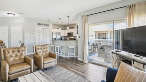A modern living room with a sofa, armchairs, a coffee table, and a TV. There is a kitchen area with a bar and a dining area with chairs. - SPC 9232 is a Beautiful recently upgraded 2 BR with Free Beach Service (Destin)