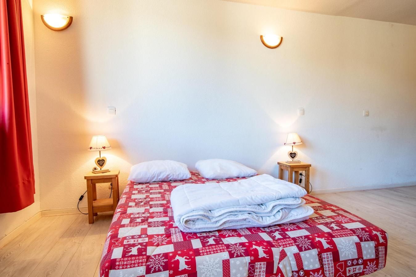 Une chambre d’hôtel avec un lit, deux tables de chevet avec des lampes et un rideau rouge.