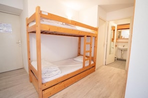 A bunk bed in a room with a wooden floor, a door, and a bathroom visible through an open door.