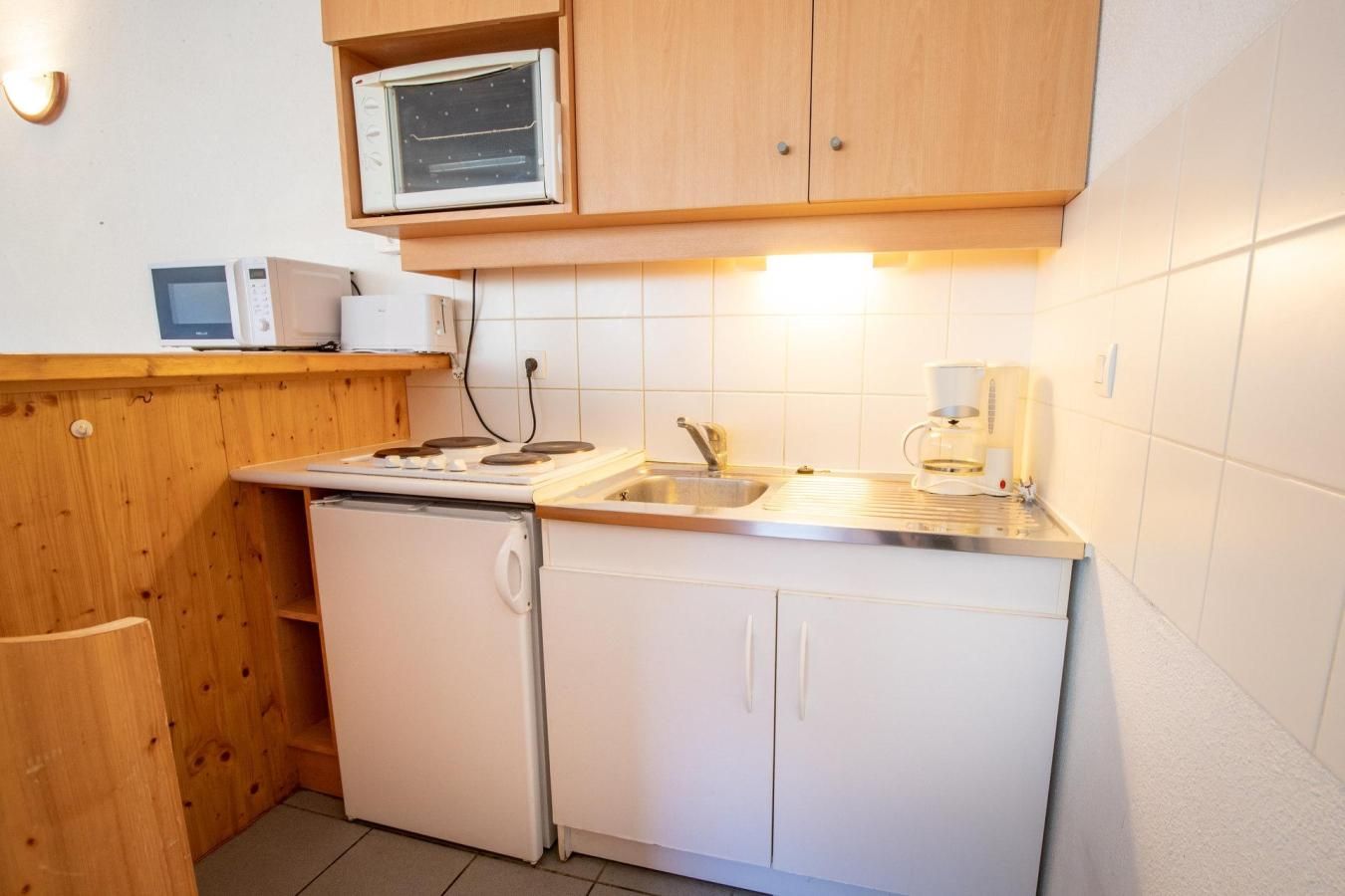 A compact kitchen with a stove, microwave, sink, and a coffee maker.