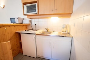 A compact kitchen with a stove, microwave, sink, and a coffee maker.