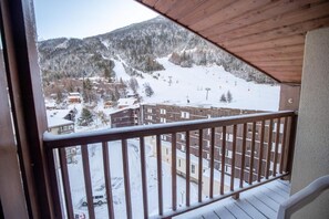 A balcony with a view of a snowy mountain landscape, including a ski slope and buildings.
