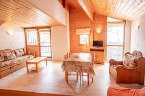 A cozy wooden cabin interior with a dining table, benches, and a sofa. - 80m from resort center, 1st floor, balcony, parking, tv, ski locker, 46m², La Norma (La Norma)