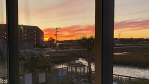 A view of a swimming pool with a fence and lounge chairs, a building in the background, and a sunset sky. - Garden City Beach- Great Location! 2 minute walk to beach and pier! Sleeps 6.  (Murrells Inlet)