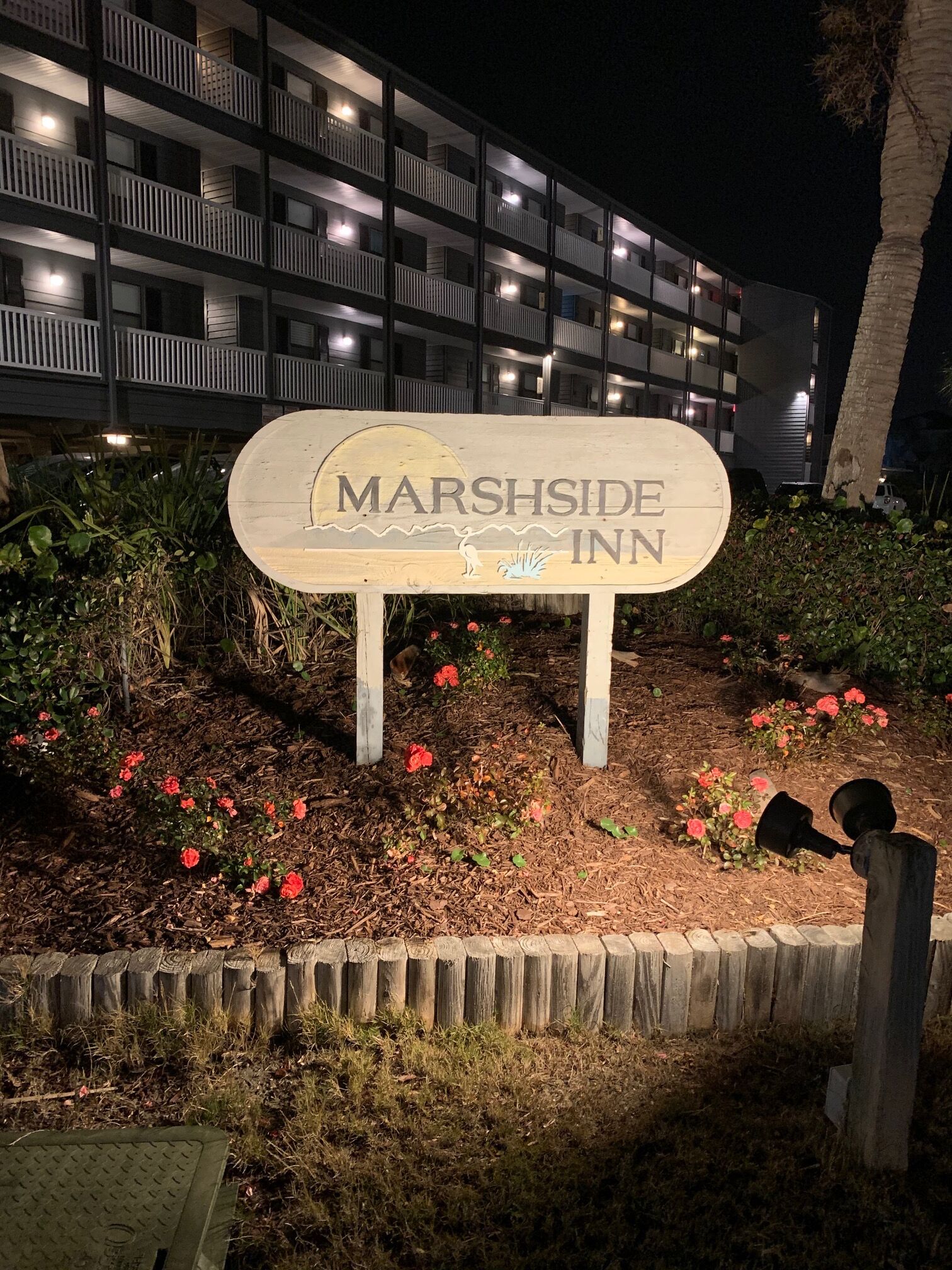 A sign for the Marshside Inn with a view of a multi-story building in the background.