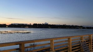 A wooden deck with metal chairs overlooking a body of water at dusk. - Garden City Beach- Great Location! 2 minute walk to beach and pier! Sleeps 6.  (Murrells Inlet)