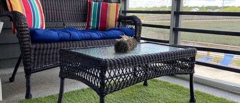 A wicker sofa with colorful cushions, a glass coffee table, and a clock on the wall.