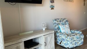 A living room with a flat-screen TV mounted on the wall, a wooden entertainment unit with a globe ornament, a patterned armchair, and a wall with motivational signs. - Garden City Beach- Great Location! 2 minute walk to beach and pier! Sleeps 6.  (Murrells Inlet)