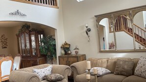 A spacious living room with a high ceiling, a ceiling fan, a large window, a staircase, and a mirrored wall. - Fully remodeled 3000sf .home with 3 bedrooms plus  and 2.5 bathrooms  (AURORA)
