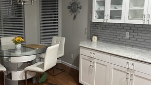 A modern kitchen with white cabinets, a granite countertop, and a dining area with a glass table and white chairs. - Fully remodeled 3000sf .home with 3 bedrooms plus  and 2.5 bathrooms  (AURORA)