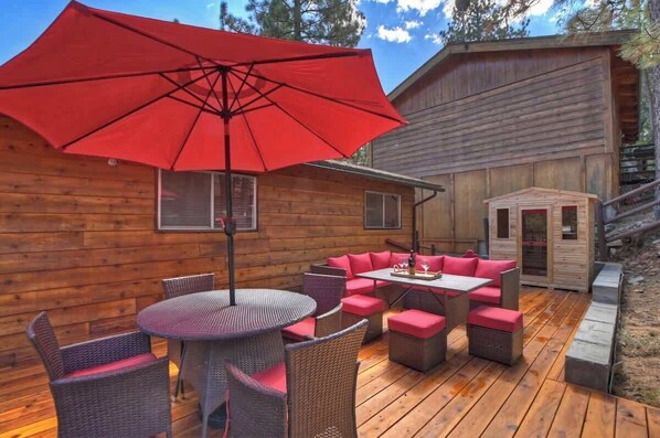A wooden cabin with a deck, a red umbrella, wicker furniture, and a small wooden structure.