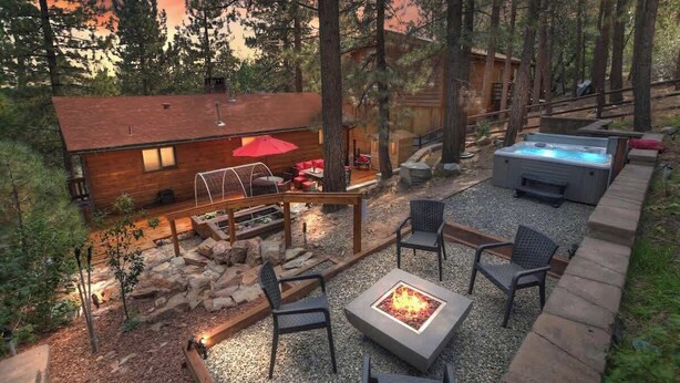 Una cabaña con jacuzzi, fogata y zona de estar al aire libre, rodeada de árboles.