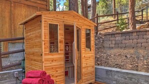 Una sauna de madera con puerta de vidrio, un banco con toallas y una pared de piedra al fondo.