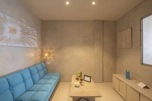 A modern room with a blue sofa, a small table with a wine bottle, and a wall-mounted light fixture.