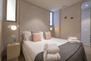 Ein ordentlich eingerichtetes Hotelzimmer mit einem großen Bett, zwei Nachttischen, einem kleinen Fenster und einer Tür.