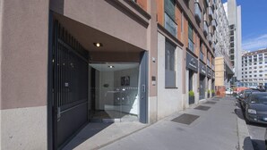 A building with a glass entrance, a visible car parked outside, and a clear sky. - Sweett | Torre Velasca VI (Milano)