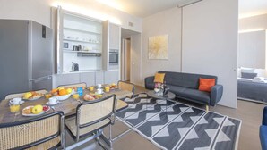 A modern living room with a dining area, a sofa, and a kitchen area with a refrigerator and microwave. - Sweett | Torre Velasca VI (Milano)