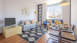 Un soggiorno moderno con un divano, un tavolo da pranzo con sedie, una TV e vista sulla città attraverso ampie finestre.
