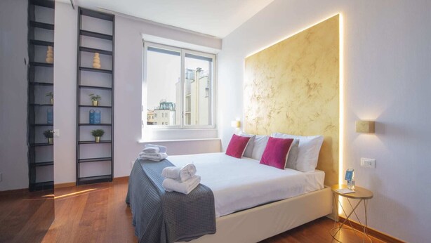 Una camera d'albergo moderna con un letto grande, un mobile contenitore a parete, una finestra con vista sulla città e una parete d'accento in marmo.